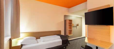 Una habitación de hotel moderna con una cama, mesita de noche, televisor y un pequeño rincón de descanso.