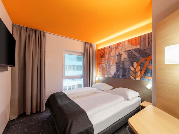 Une chambre d’hôtel avec un lit, un bureau, une télévision et une fenêtre avec des rideaux.