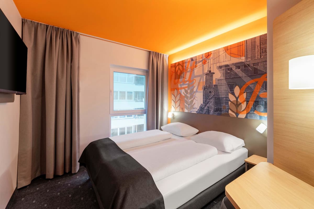 Une chambre d’hôtel avec un lit, un bureau, une télévision et une fenêtre avec des rideaux.