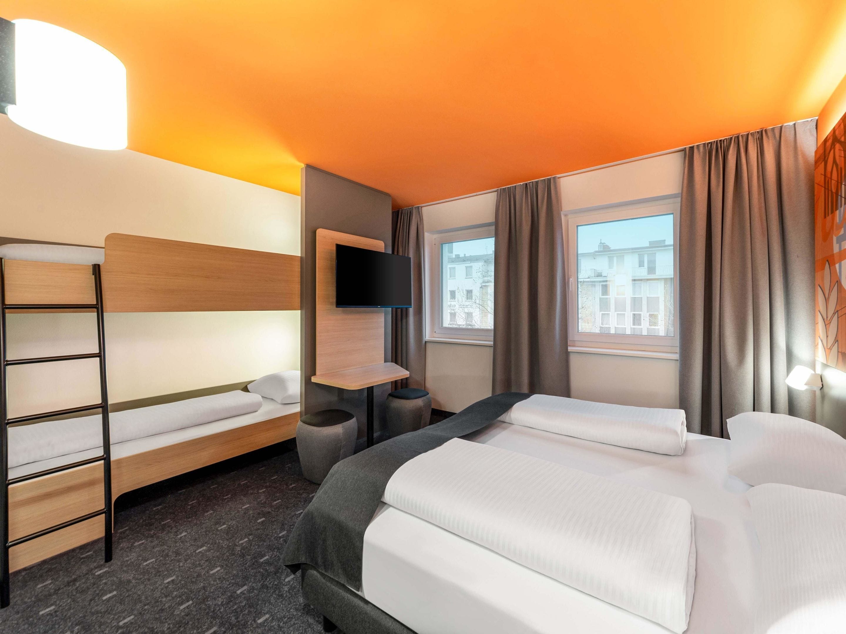 Une chambre d’hôtel avec un lit superposé, un bureau, un téléviseur à écran plat et une fenêtre avec des rideaux.