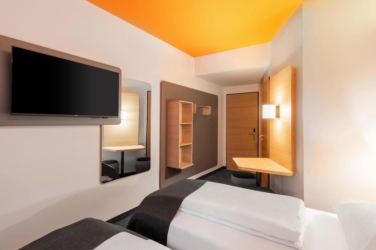 Une chambre d’hôtel avec deux lits, une télévision, un miroir et une armoire.