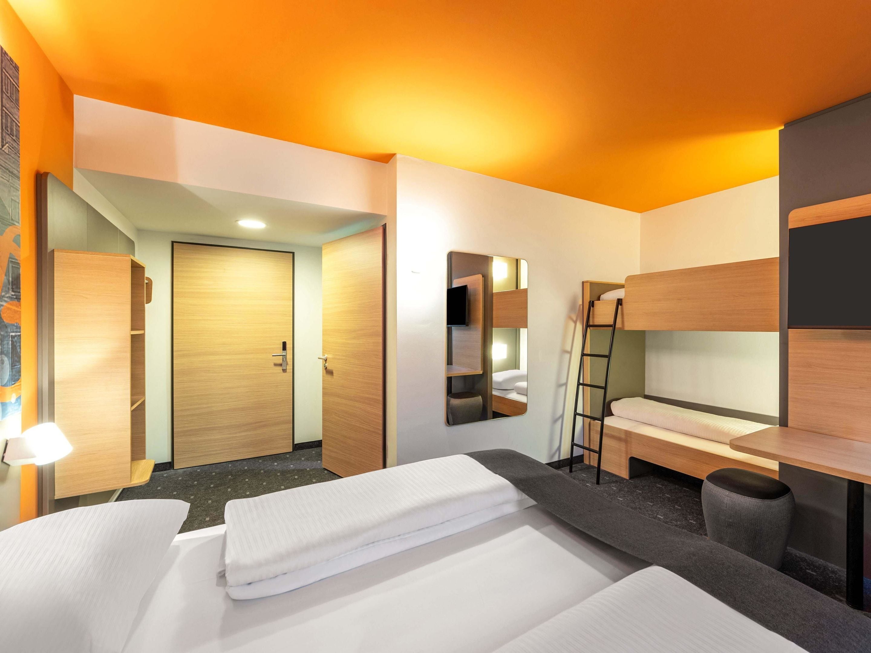 Een hotelkamer met een stapelbed, een bureau, een stoel, een spiegel en een kledingkast.