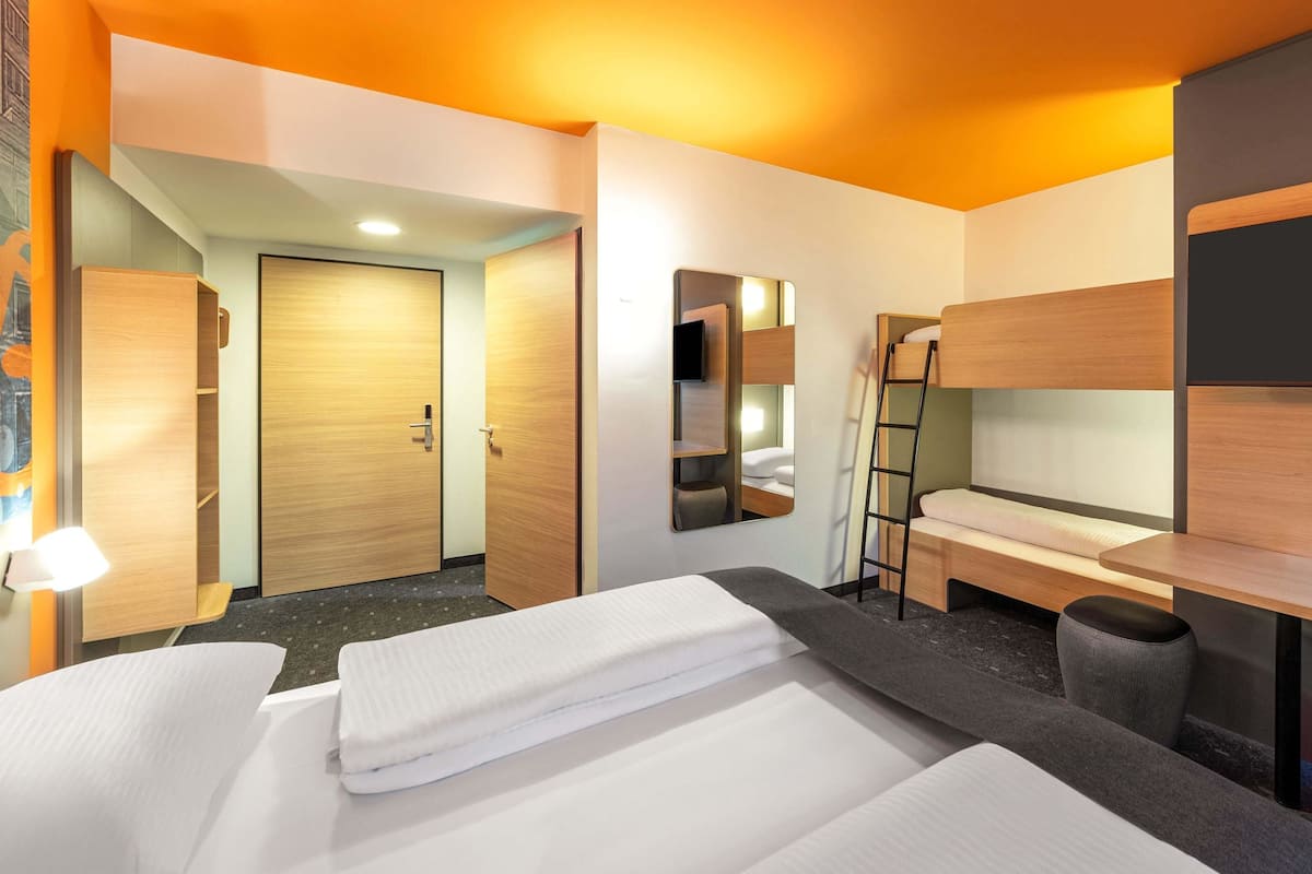 Une chambre d’hôtel équipée d’un lit superposé, d’un bureau, d’une chaise, d’un miroir et d’une armoire.