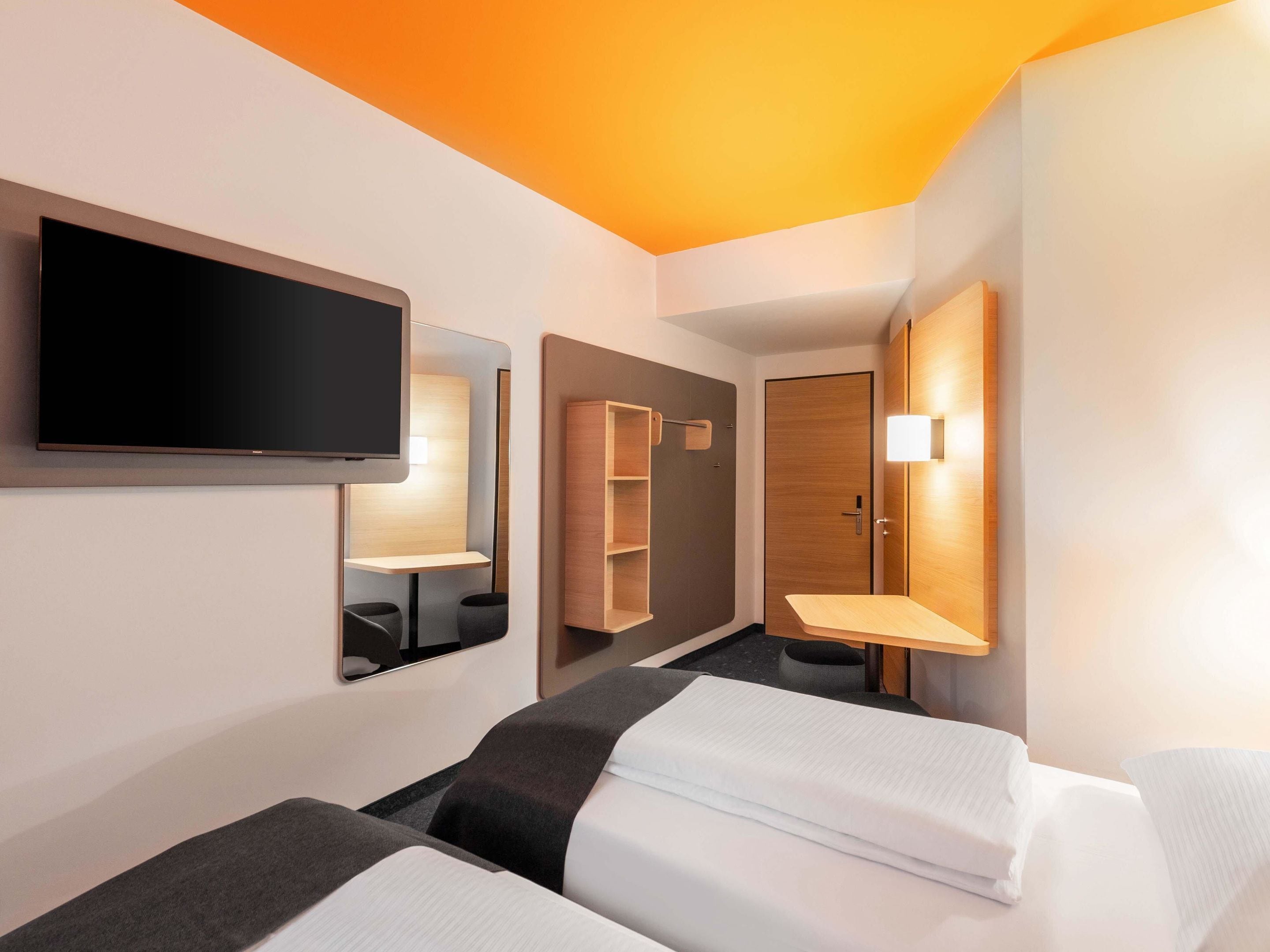 A hotel room with two beds, a TV, a mirror, and a wardrobe.