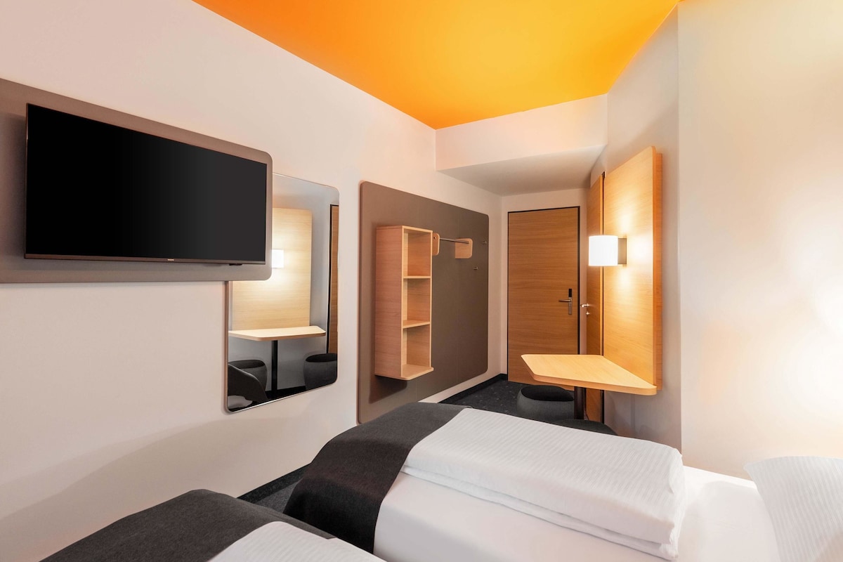 Une chambre d’hôtel avec deux lits, une télévision, un miroir et une armoire.