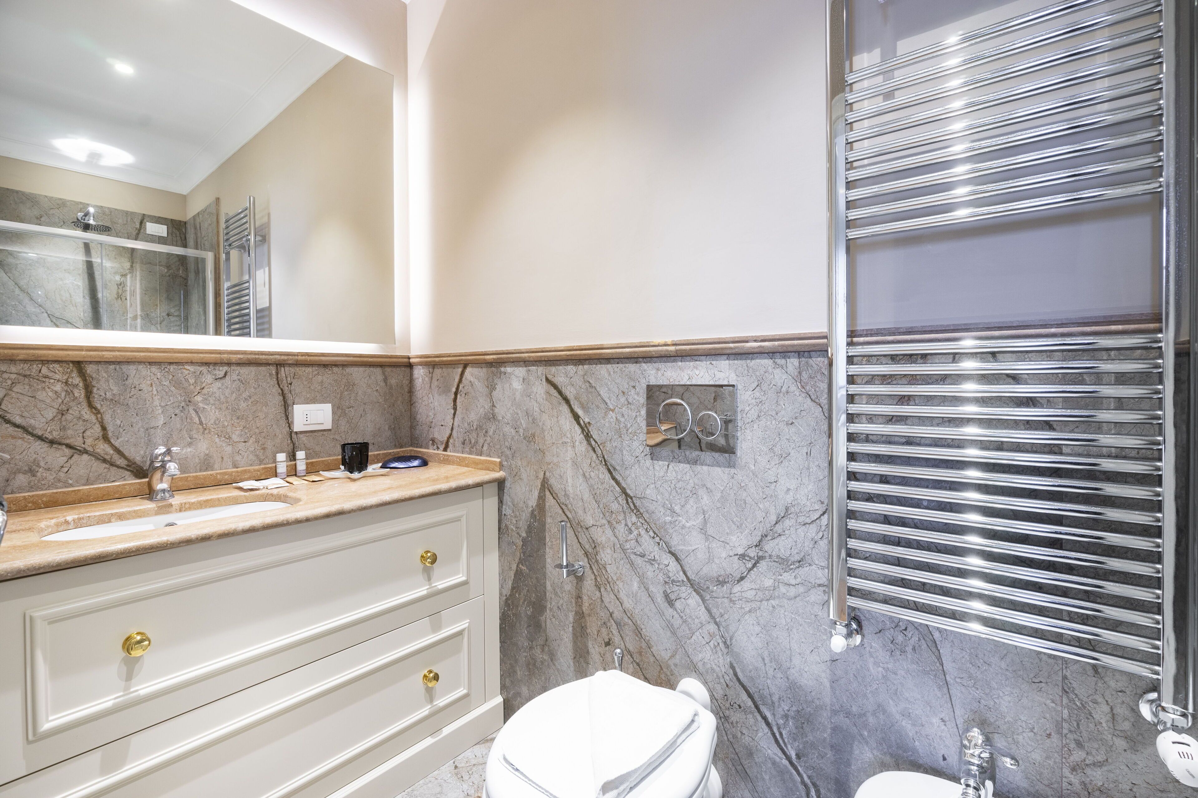 Ein Badezimmer mit Marmorplatte, Toilette in Weiß und einem chromfarbenen Handtuchhalter.