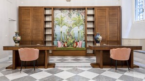 Zona pranzo con pavimento a scacchi, due sedie rosa, un tavolo in legno e una parete decorata con un murale tropicale.