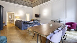 Un'ampia stanza con un tavolo da pranzo in legno, sedie viola, un divano e un televisore montato a parete.