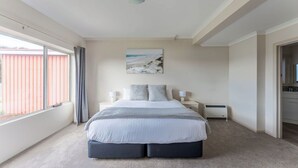 A bedroom with a large bed, a window with curtains, a wall-mounted artwork, and a bedside table with a lamp. - Cosy and Comfortable Unit with Parking & Wifi (Devonport)