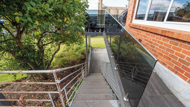 A staircase leading to a building with a glass railing, surrounded by greenery and a tree with fruit. - Cosy and Comfortable Unit with Parking & Wifi (Devonport)