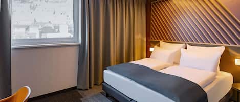 Habitación de hotel moderna con una cama grande, vistas de edificios a través del ventanal y un diseño de techo singular.