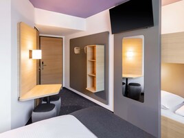 Una habitación de hotel moderna con cama, escritorio, silla, televisor y estante con espacio de almacenamiento.