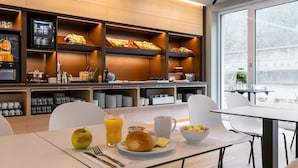 Een moderne ontbijtruimte met een buffet, eettafels en uitzicht op het omliggende landschap.
