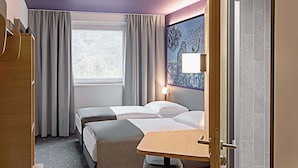 Een hotelkamer met twee bedden, een bureau, een stoel en een raam met gordijnen.