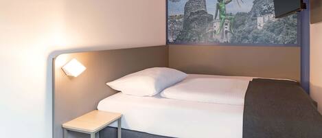 A modern hotel room with a bed, a small bedside table, a wall-mounted TV, and a painting of a landscape.