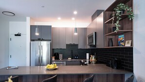 A modern kitchen with a central island, stainless steel appliances, and a dark backsplash. - Modern 2 Bedroom Condo with Workspace (Revelstoke)