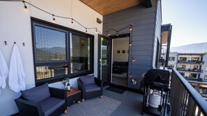 A balcony with a sofa, a small table, and a grill. - Modern 2 Bedroom Condo with Workspace (Revelstoke)
