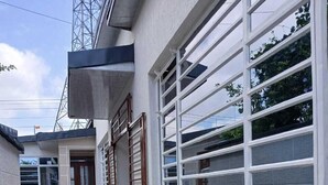 Un couloir au sol carrelé, une porte et une fenêtre munie d’une grille métallique.