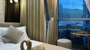 A hotel room with a bed, pillows, a window with curtains, a view of the city, and a small table with a tray.