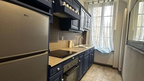 Une cuisine moderne avec des meubles de couleur sombre, un réfrigérateur en acier inoxydable, un four encastré et une fenêtre ornée de rideaux légers.