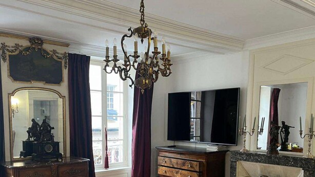 Un salon spacieux doté d’un parquet en bois, d’un lustre, d’une télévision, d’une cheminée et d’un grand miroir.