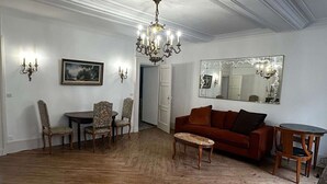 Un salon spacieux doté d’un parquet en bois, d’un canapé rouge, d’une table à manger avec des chaises, d’un lustre et d’un grand miroir mural.