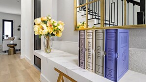 A marble console table with a vase of yellow flowers, three vintage bookshelf editions of Monopoly, Scrabble, and Clue, and a mirror with a gold frame reflecting a staircase.