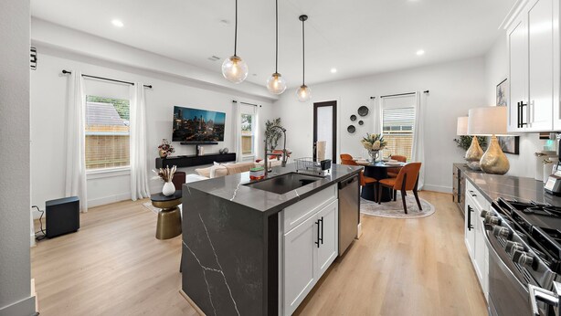 A modern kitchen with a central island, pendant lighting, and a dining area with a table and chairs.