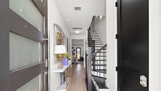 Un pasillo moderno con una escalera, una puerta con cerradura electrónica y un estante con objetos decorativos.