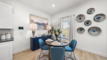 A dining area with a round table, blue chairs, white plates, and a vase of flowers.
