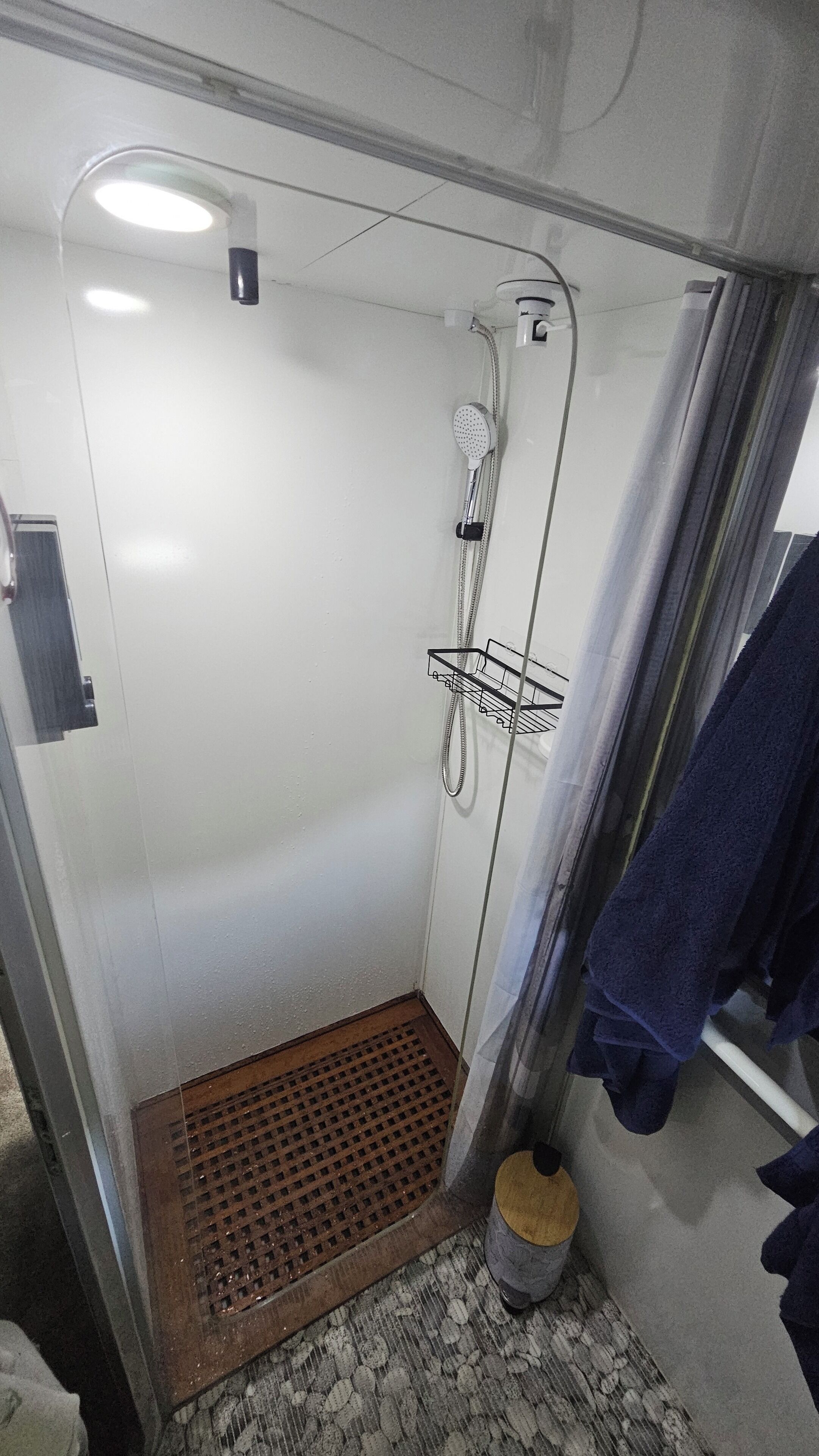 A small, enclosed shower area with a showerhead, a towel rack, and a drain.