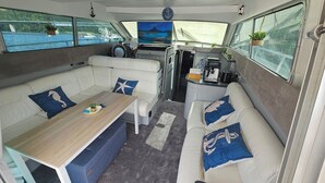 A boat interior with a dining area, a kitchen, and seating with views of the water. - Unusual nights on a 12m boat in the heart of nature (Loire gorges)  (Bully)