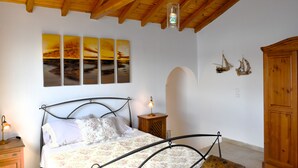 A bedroom with a bed, wooden headboard, a nightstand, a lamp, a wooden cabinet, and wall art.
