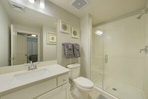 A bathroom with a white sink, toilet, and glass shower enclosure. There are two towels hanging on the wall.