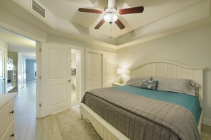 A bedroom with a bed, a ceiling fan, a nightstand, and a door leading to another room.