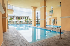 A swimming pool with tiled flooring and a metal handrail, surrounded by beige walls and columns.