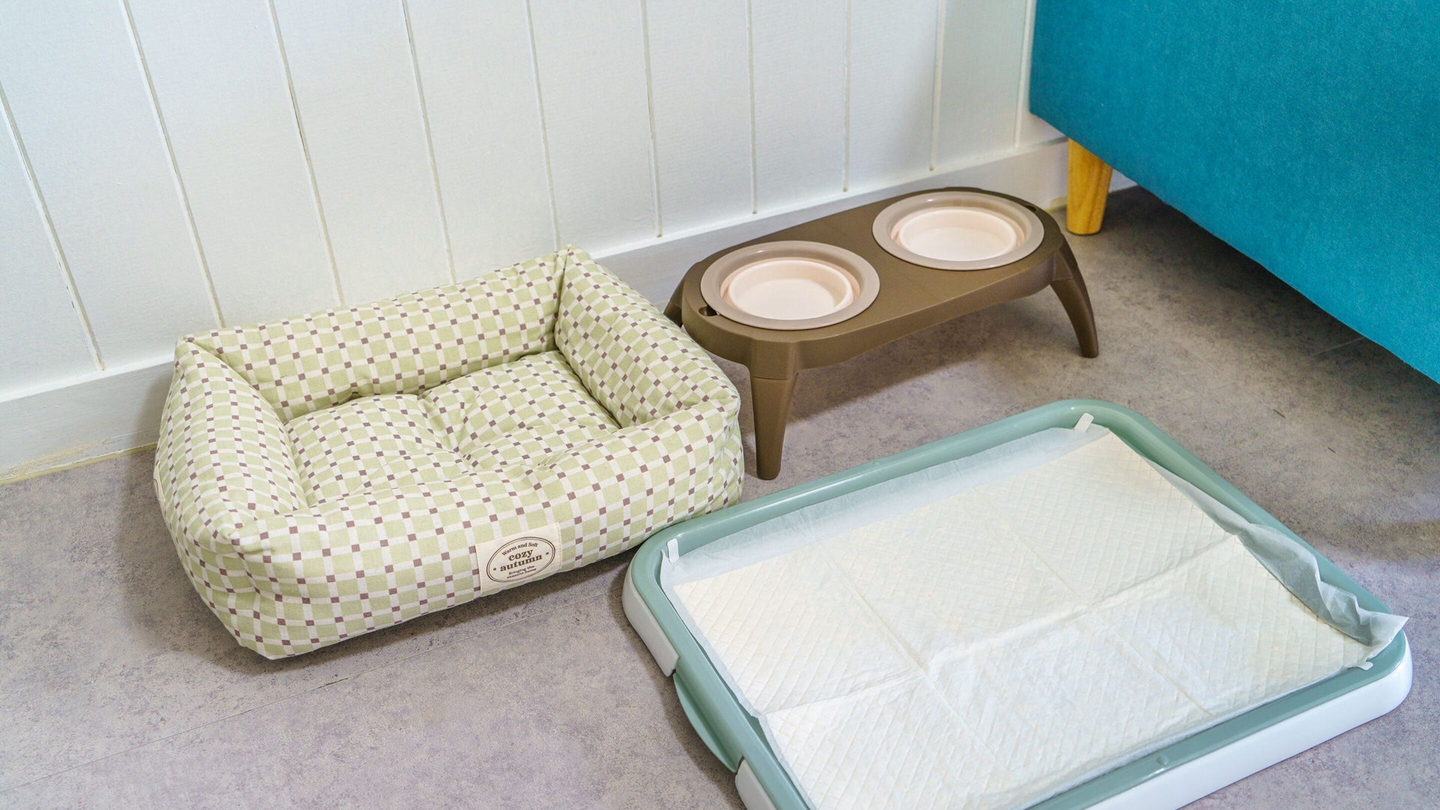 Una cama para mascotas, dos comederos y un tapete para mascotas en el suelo.