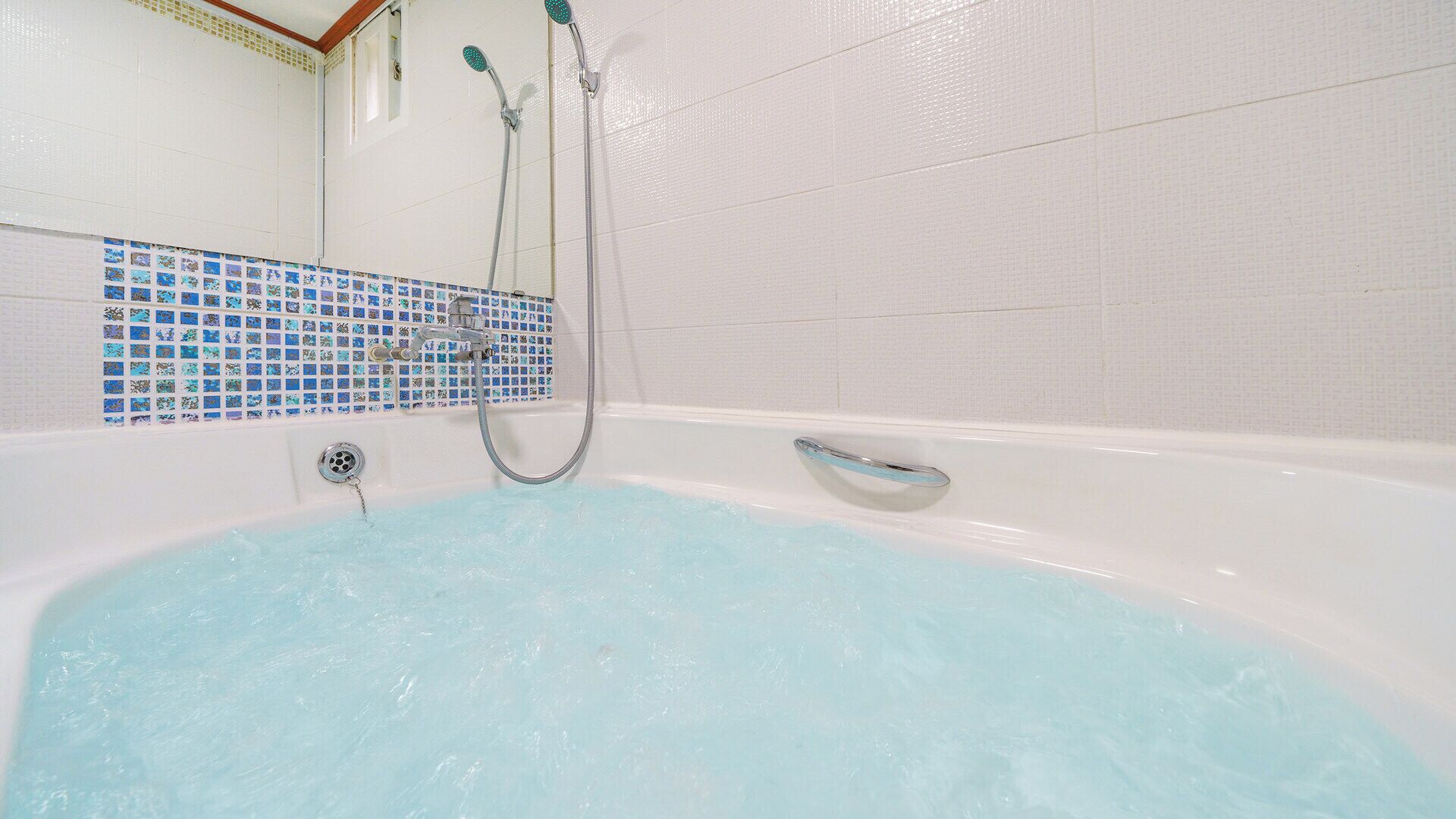Una bañera con ducha y desagüe, un muro de azulejos con diseño de mosaico y una ventana con molduras de madera.