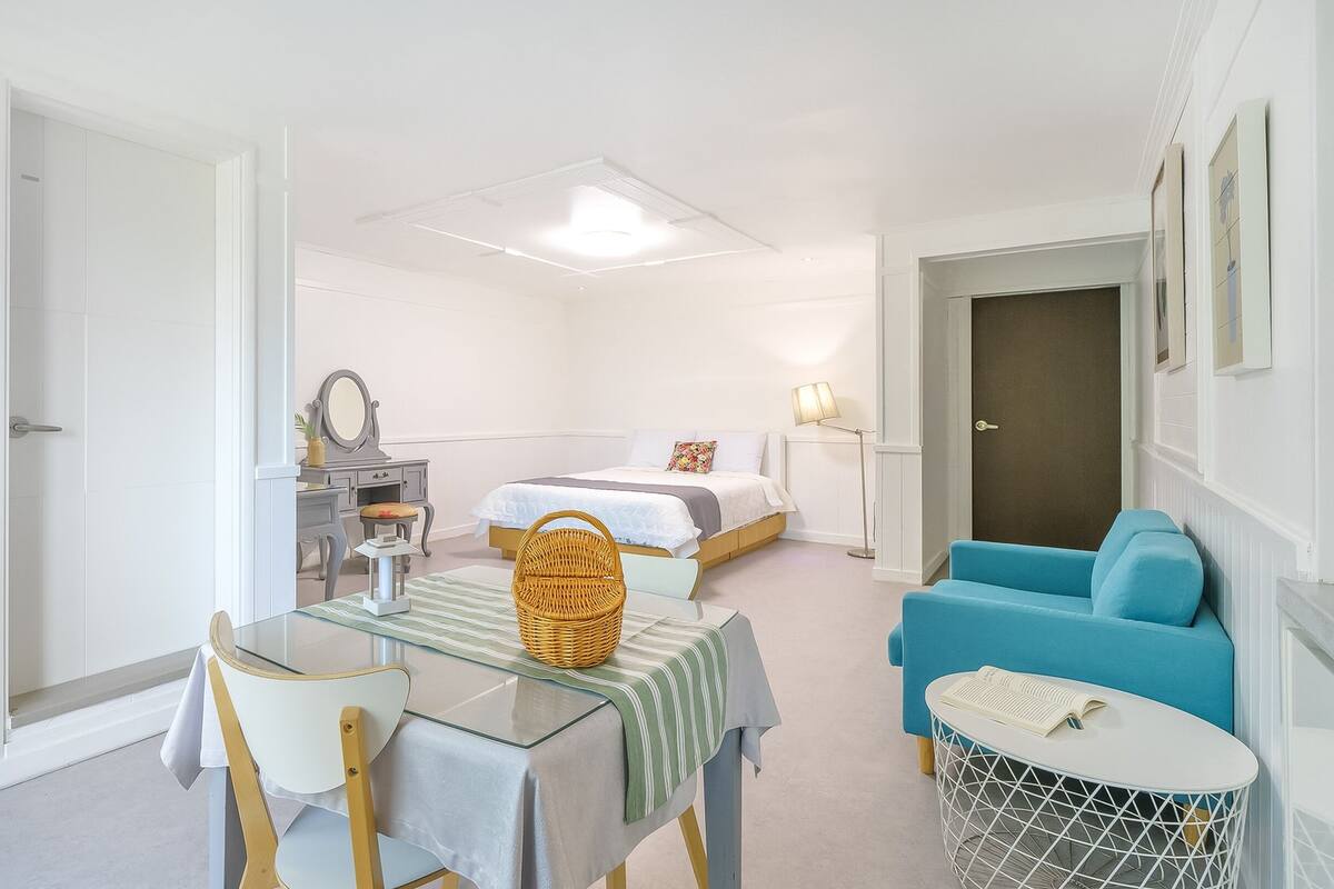 A compact room with a bed, a blue sofa, a dining table with chairs, and a small side table.