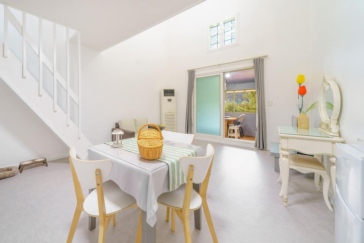 A dining area with a table set for two, a wicker basket, and a view of a balcony with a chair.