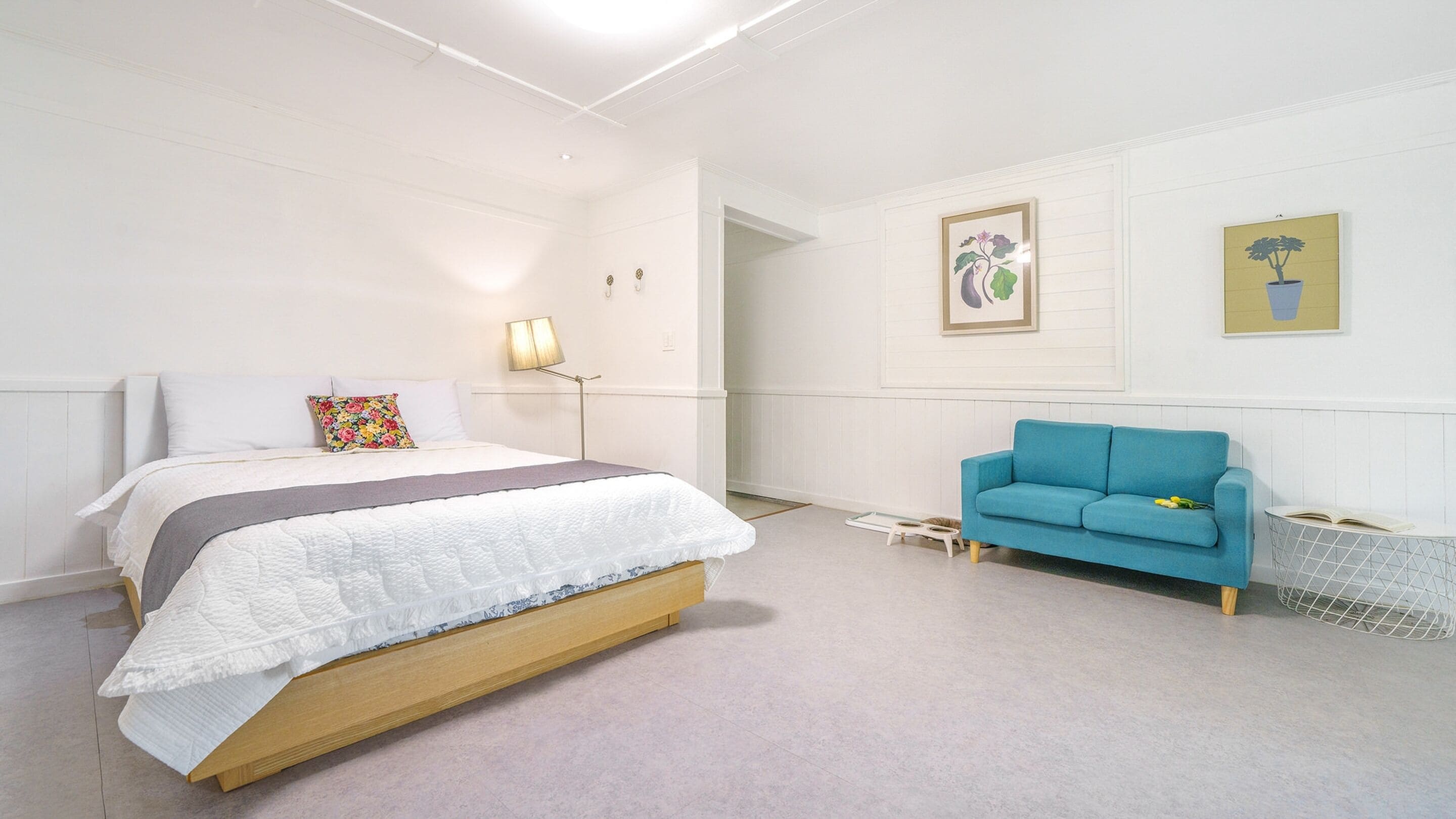 A bedroom with a bed, a blue sofa, a lamp, and two framed pictures on the wall.