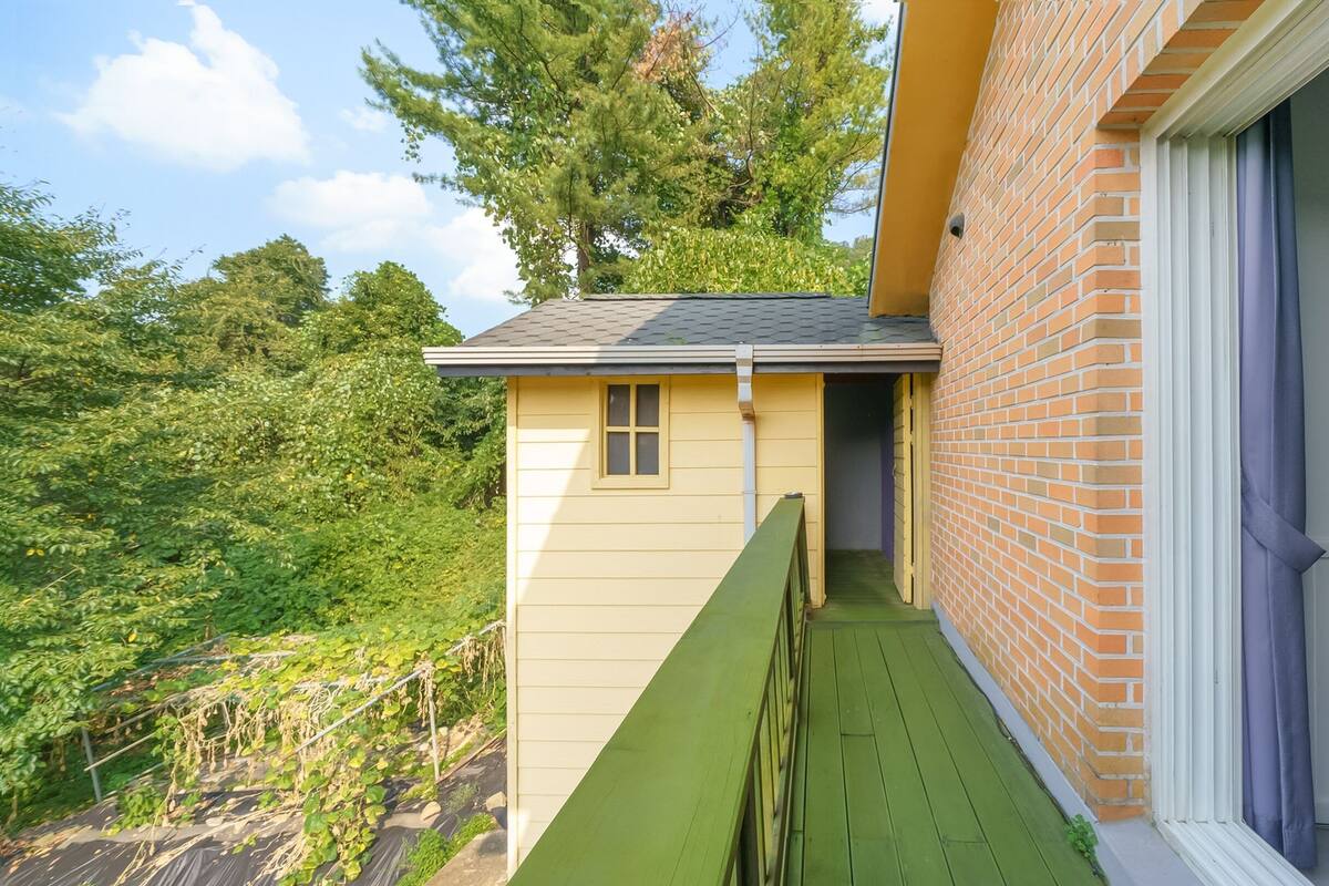 A small, yellow building with a green deck, adjacent to a brick wall and a sliding glass door.