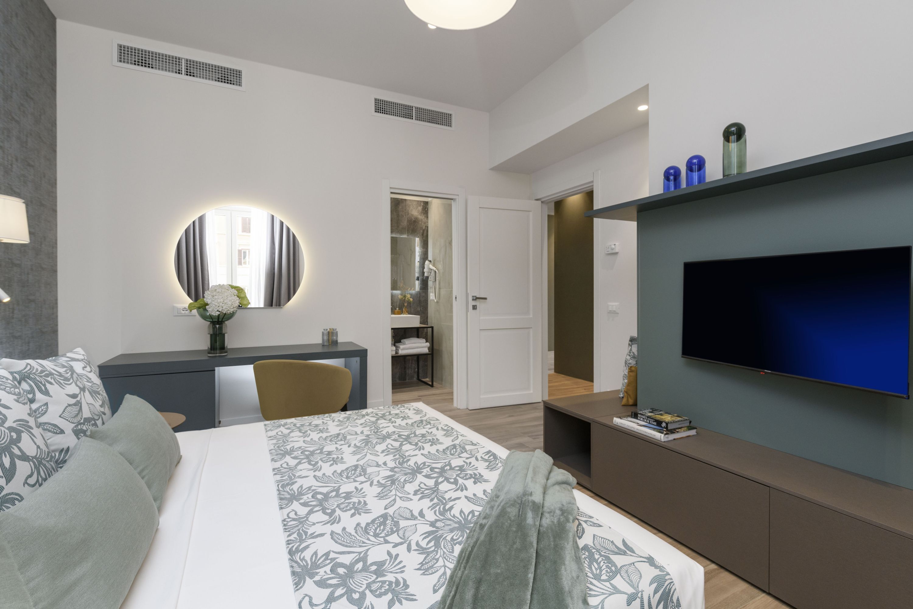 Een moderne hotelkamer met een groot bed, een televisie, een bureau met een spiegel, en een badkamer zichtbaar door een open deur.