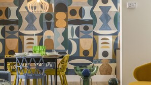 A dining area with a geometric patterned wall, a table set with plates and glasses, and chairs with a blue and yellow color scheme. - Domus Augustea - Nerone (Rome)