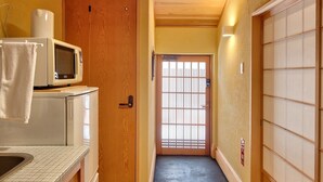 A narrow hallway with a wooden door and a sliding glass door at the end. A microwave is visible on a counter to the left. - Connect inn Kyotogojo (Kyoto)