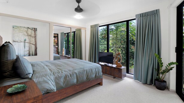 A modern bedroom with a large bed, a TV, and a view of greenery outside.