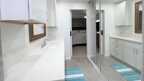 Een moderne badkamer met een wit wastafelmeubel, spiegel en kastjes. Boven het wastafelmeubel hangt een spiegel met houten lijst en op de vloer ligt een vloerkleed met blauwe strepen.