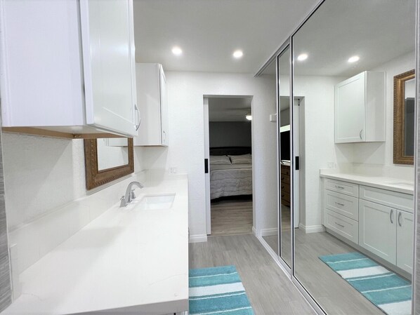 Une salle de bain moderne avec un lavabo blanc, un miroir et des meubles de rangement. Un miroir à cadre en bois est placé au-dessus du lavabo, et un tapis à rayures bleues recouvre le sol.
