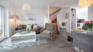 A modern living room with a sofa, a glass coffee table, a wicker chair, and a dining area with a table and chairs. - Silbermöwe - Rooftop Terrace with Panoramic Views, First Row Waterfront, Firepla (Olpenitz)