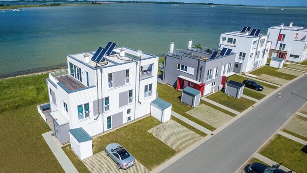 A modern apartment complex with multiple buildings, a parking area, and a view of the sea. - Silbermöwe - Rooftop Terrace with Panoramic Views, First Row Waterfront, Firepla (Olpenitz)